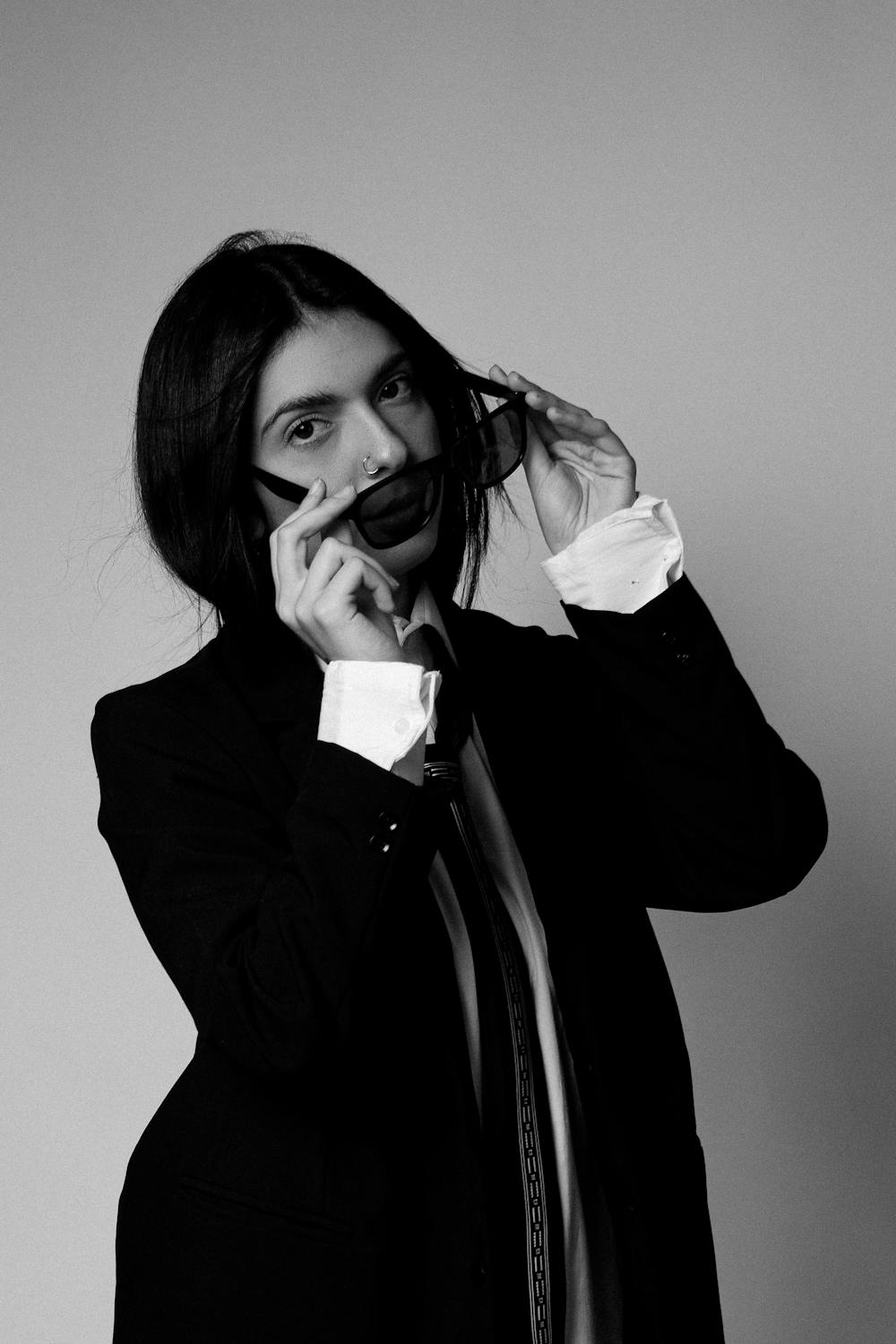 Black and white portrait of a model in a suit lifting sunglasses.