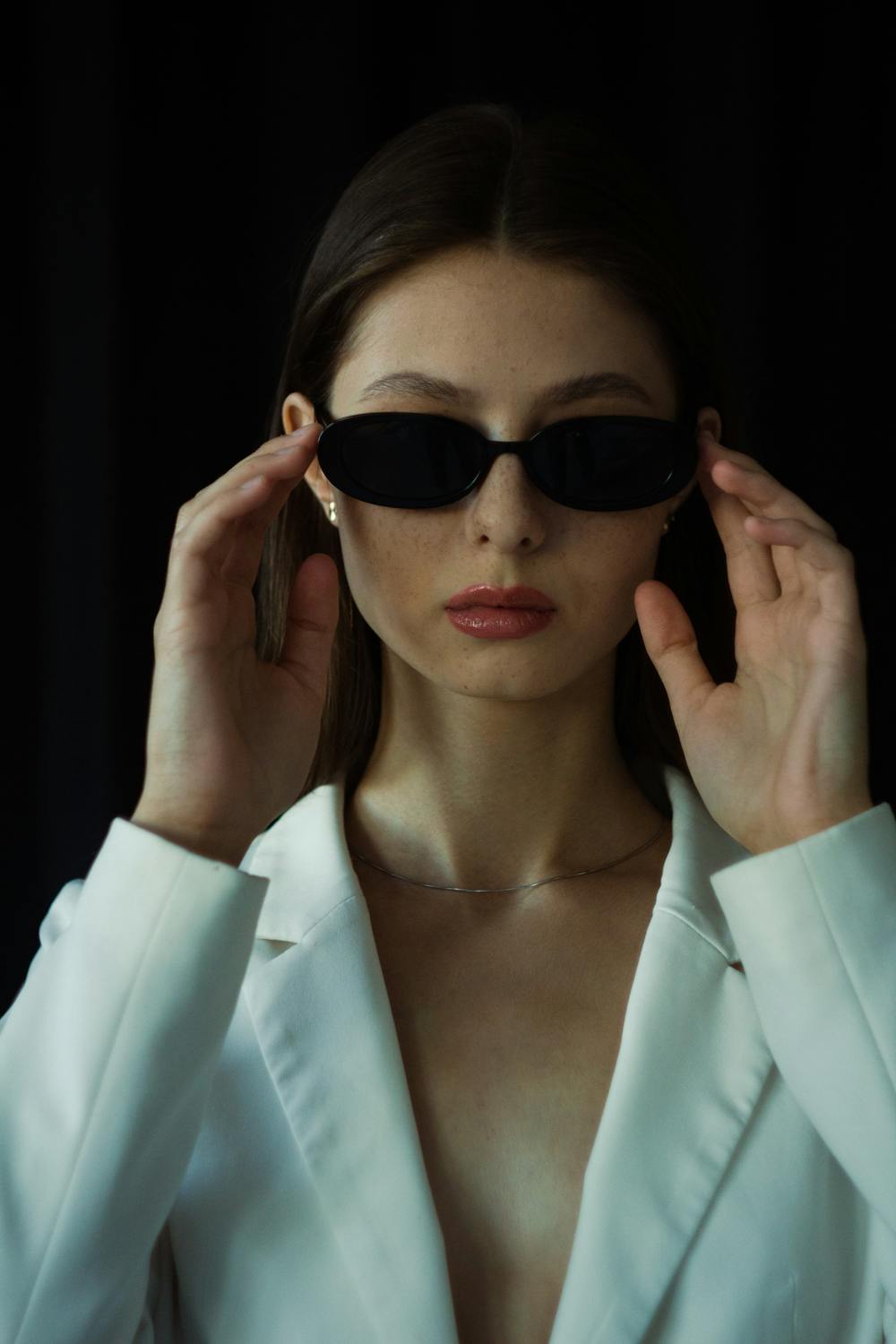 Studio portrait of a model in dark sunglasses and a white blazer.