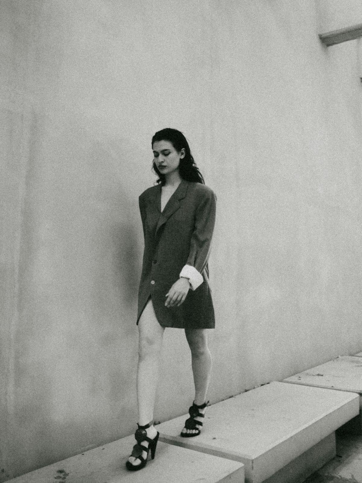 Model walking along a concrete wall in an editorial outfit.